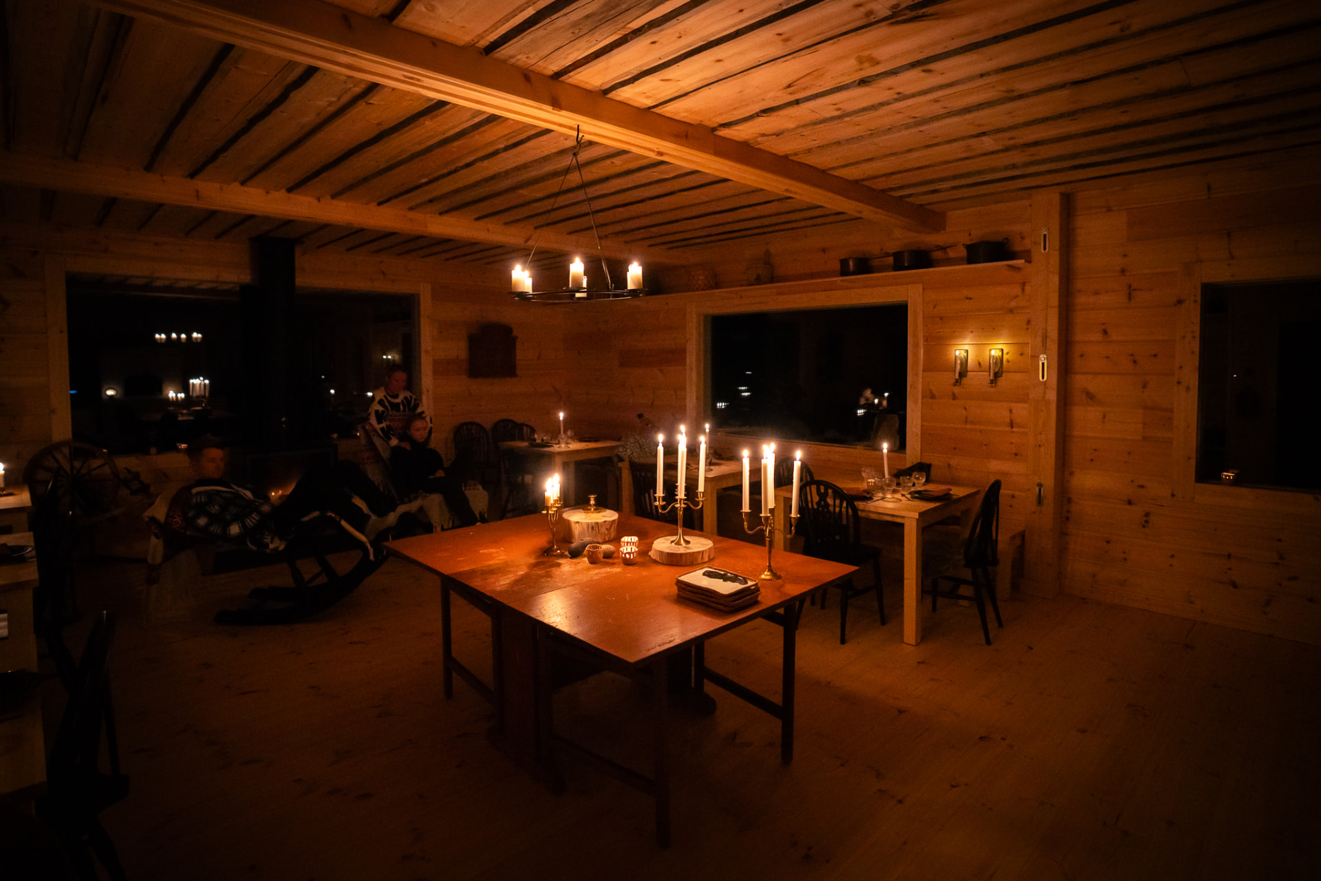 Candlelit cabin dining room at night, guests resting by the hearth