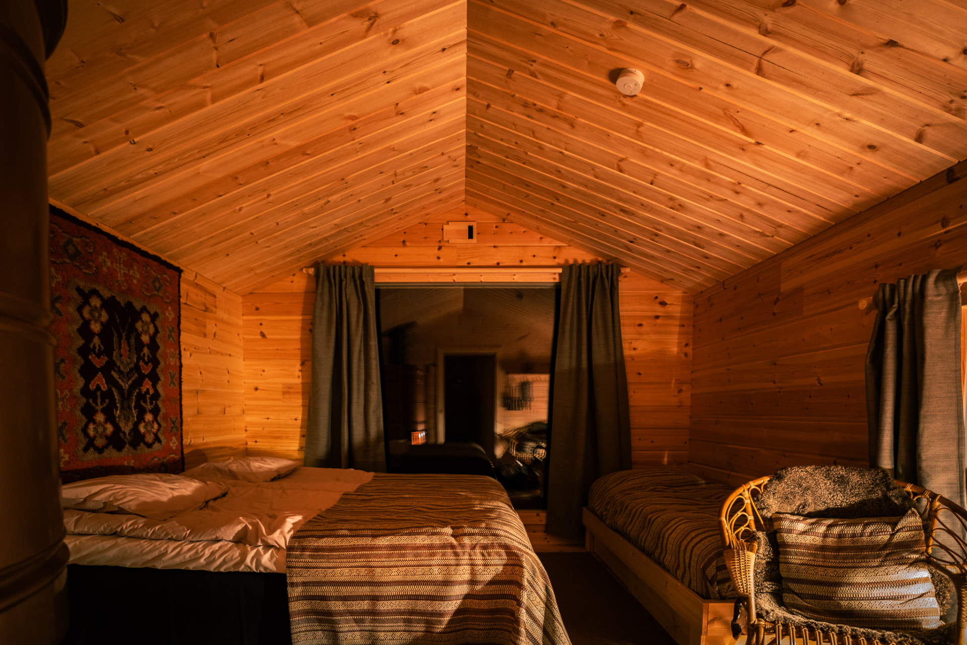 Pine-wood cabin bedroom with a made bed and a wicker chair