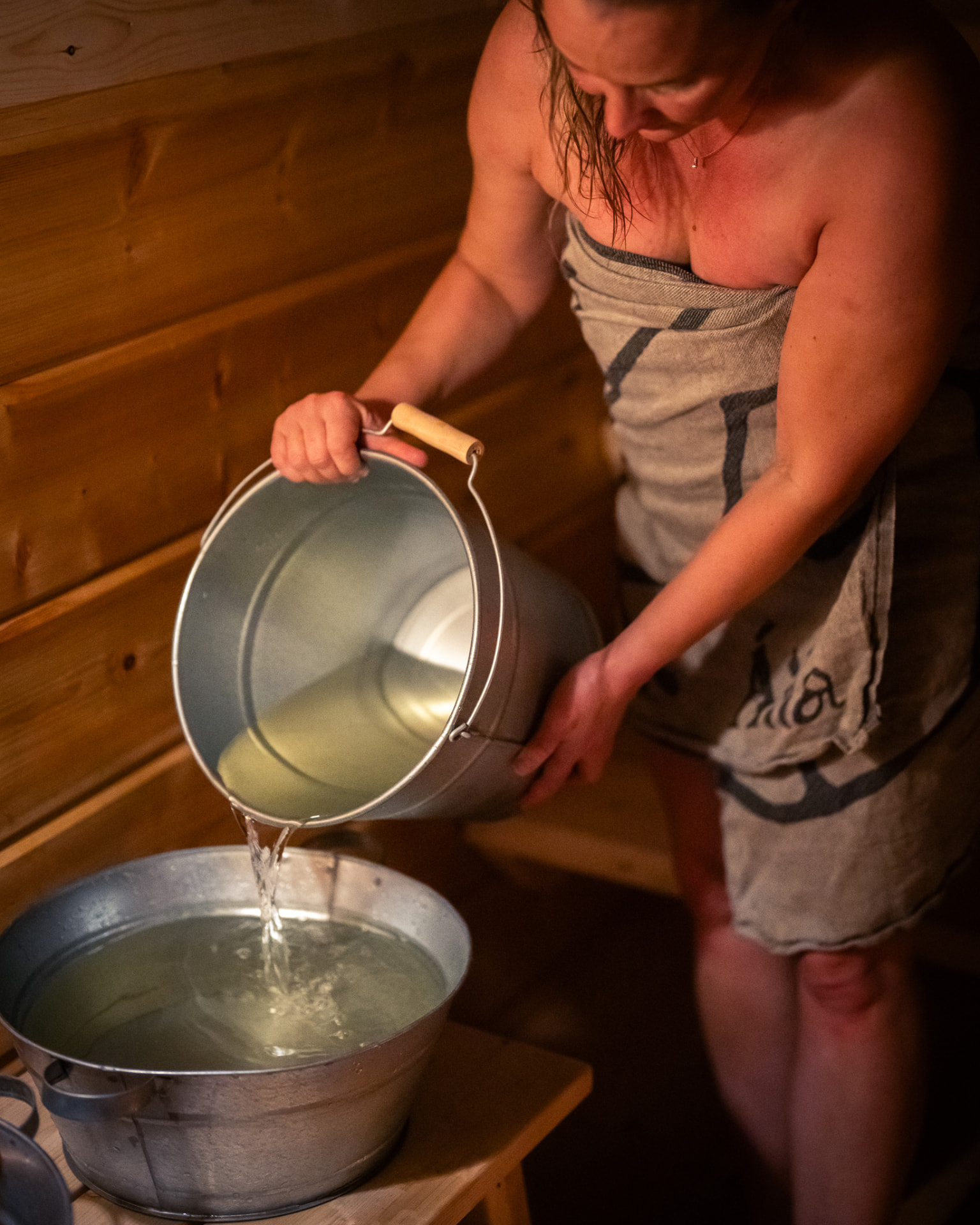 A guest pouring water from a zinc pail into a wash basin in the sauna