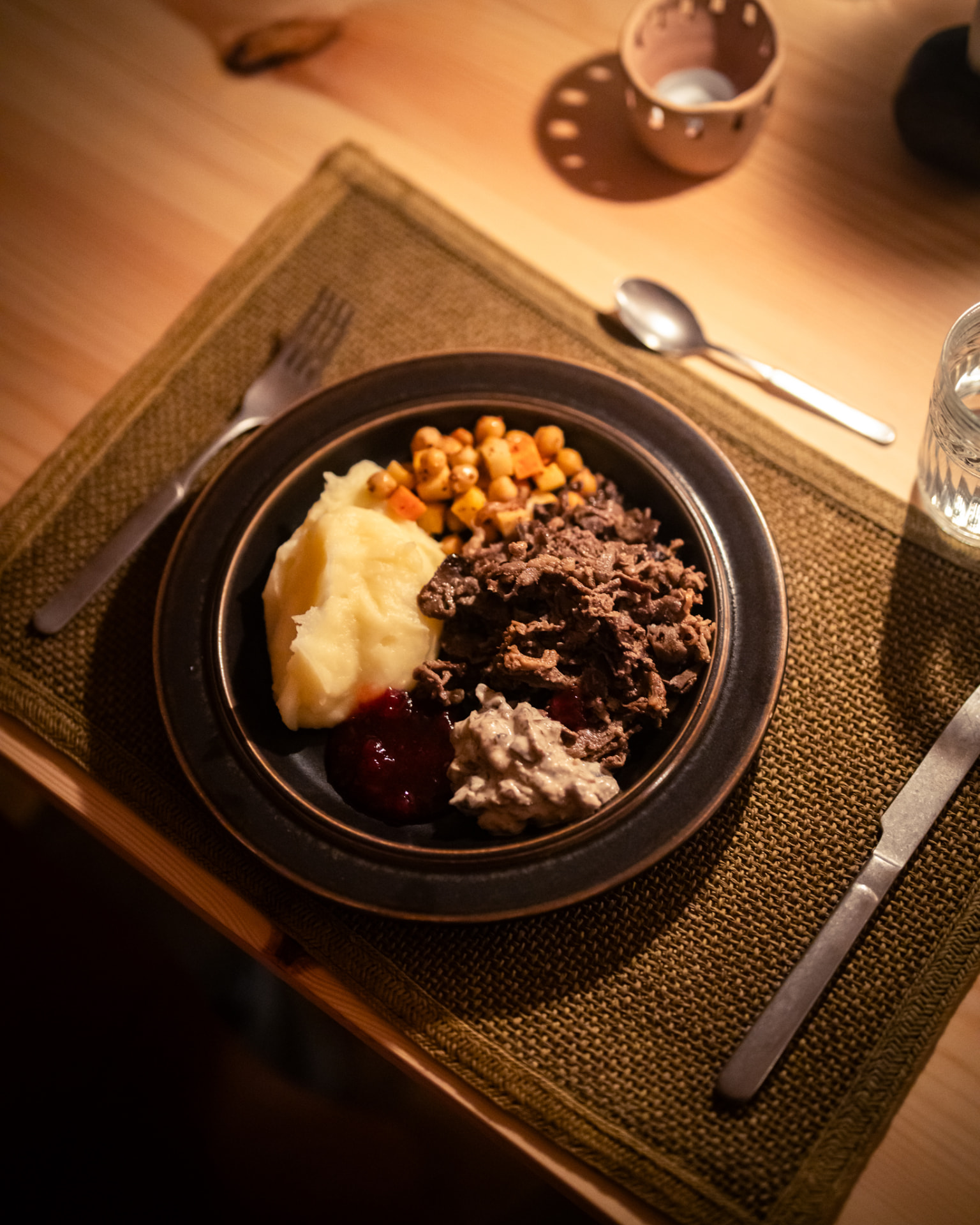 A plate of mashed potatoes, sautéed meat, roasted vegetables and lingonberries on a woven placemat