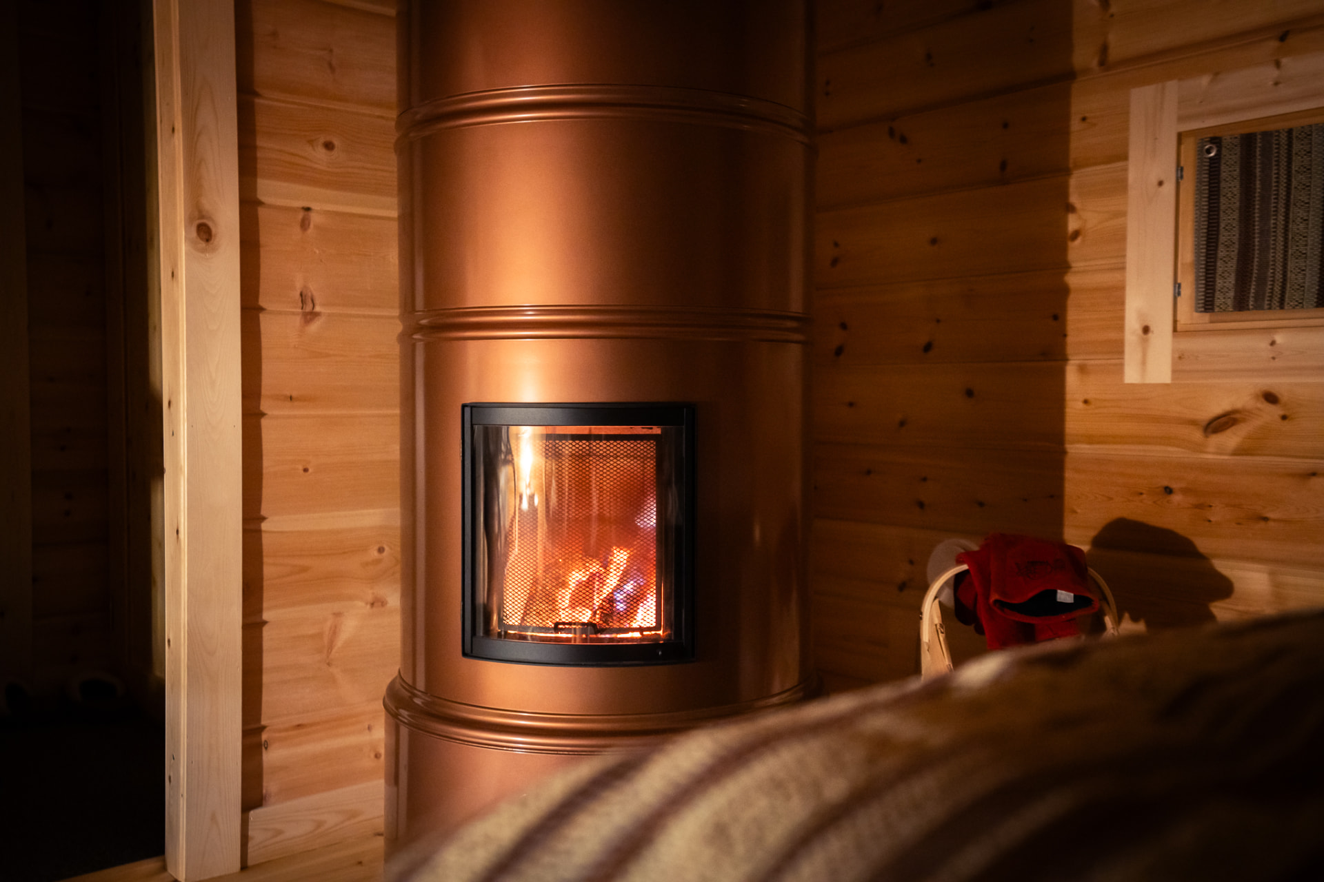 A copper wood-burning stove with flames glowing inside a log cabin